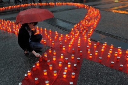 Sur cette photo, tu peux voir une femme qui allume une des bougies qui forment un ruban rouge. Ce ruban rouge symbolise la lutte contre le sida.( © AFP PHOTO / ALEXA STANKOVIC)