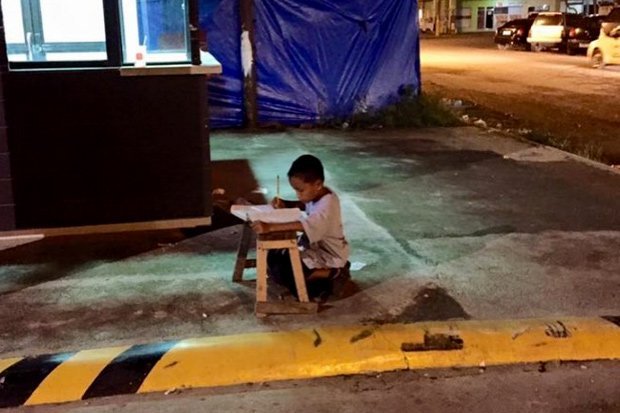 Daniel faisant ses devoirs dans la rue, à la lumière d'un magasin.