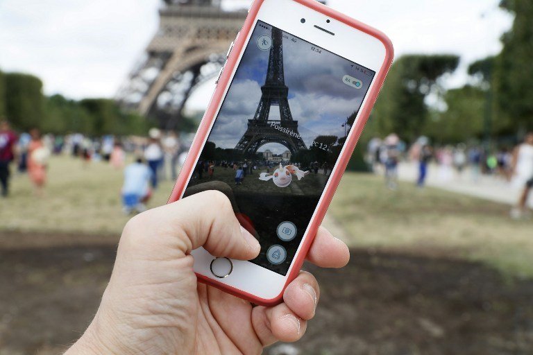 TO GO WITH AFP STORY BY ERWAN LUCAS (FILES) This file photo taken on July 26, 2016 shows the "Pokemon Go" app on the screen of a mobile phone, next to the Eiffel Tower in Paris. The global Pokemon Go craze has prompted a slew of complaints, from memorial sites arguing it's disrespectful to play there to whole countries imposing a ban on the smartphone game. But is it really possible to declare a place a no-go zone for people hunting the cartoon monsters? / AFP PHOTO / Thomas SAMSON