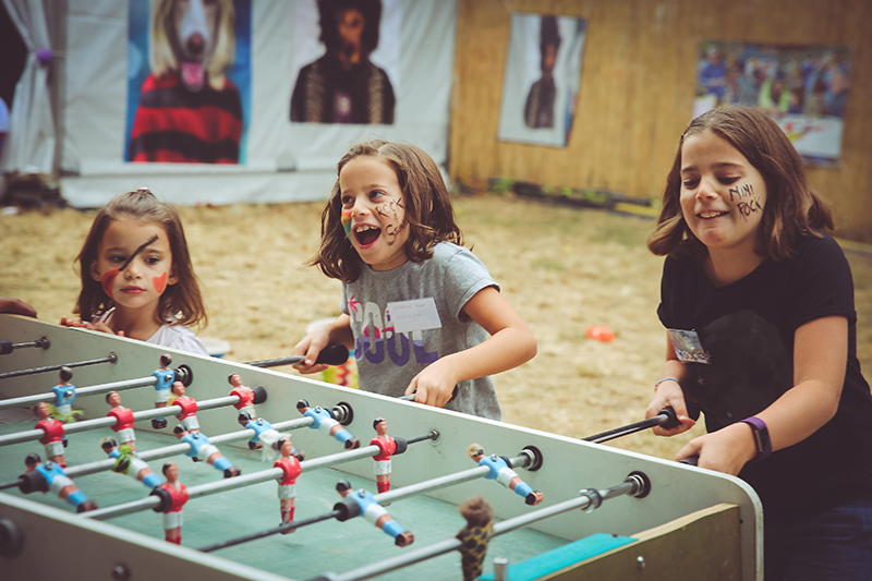 Des enfants jouant au babyfoot. Leurs visages sont maquillés aux couleurs de Rock en Seine