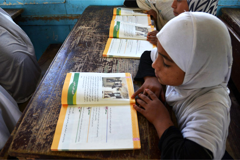 jeune Afghane lisant un manuel scolaire en classe. 