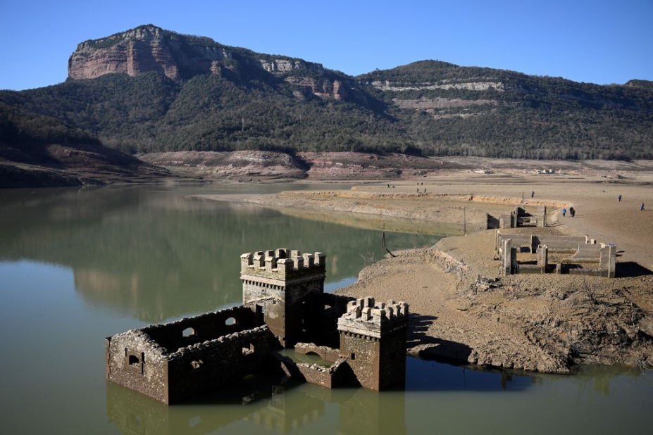 Un château est à moitié immergé par l'eau d'un très grand lac. Sur le bord du lac, des promeneurs.