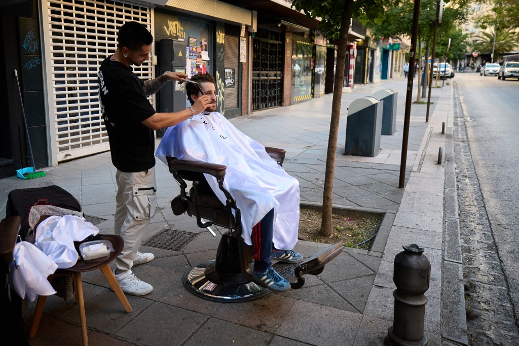 Un coiffeur s'est installé dans la rue avec son client et lui coupe les cheveux à la lumière du jour.