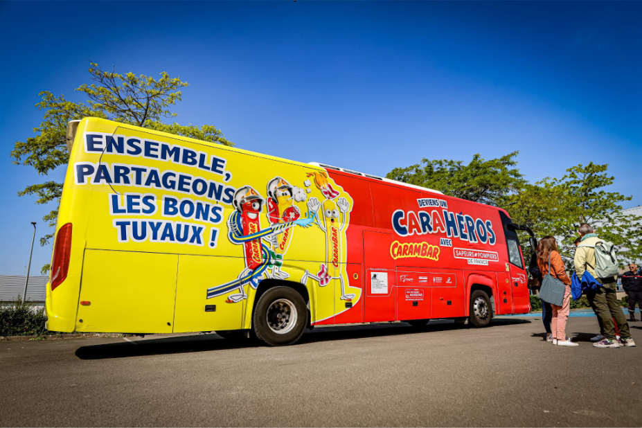 Bus des pompiers floqué aux couleurs des carahéros, avec les mascottes dessinées dessus .