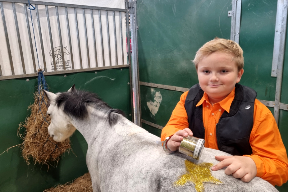 Stuart dans le box de son poney. Il vient de lui dessiner une étoile sur le dos. Elle est faite avec des paillettes dorées. 