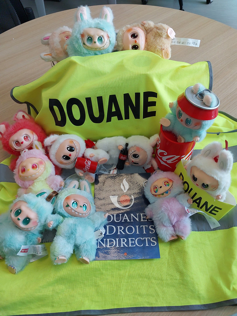 Sur un gilet jaune écrit "DOUANE", sont posés plusieurs peluches Labubu contrefaites.