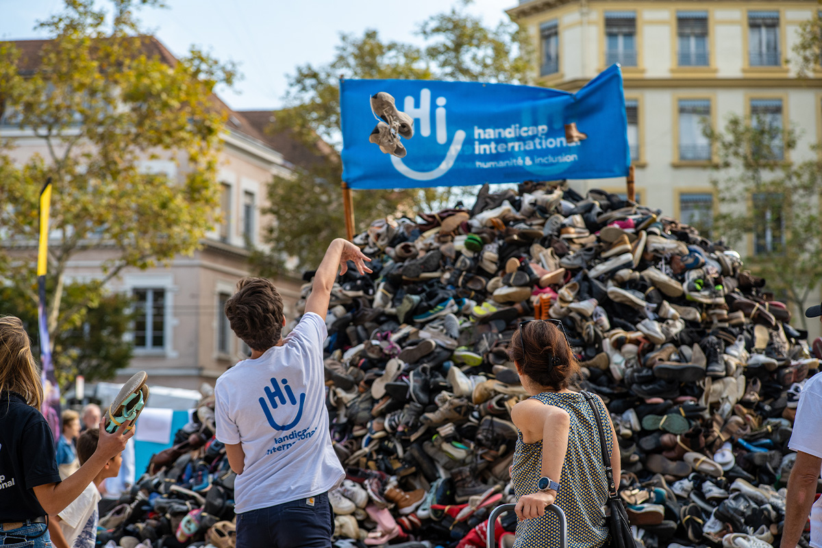 deux personnes jetant des chaussures sur une pyramide de chaussures d'Handicap international