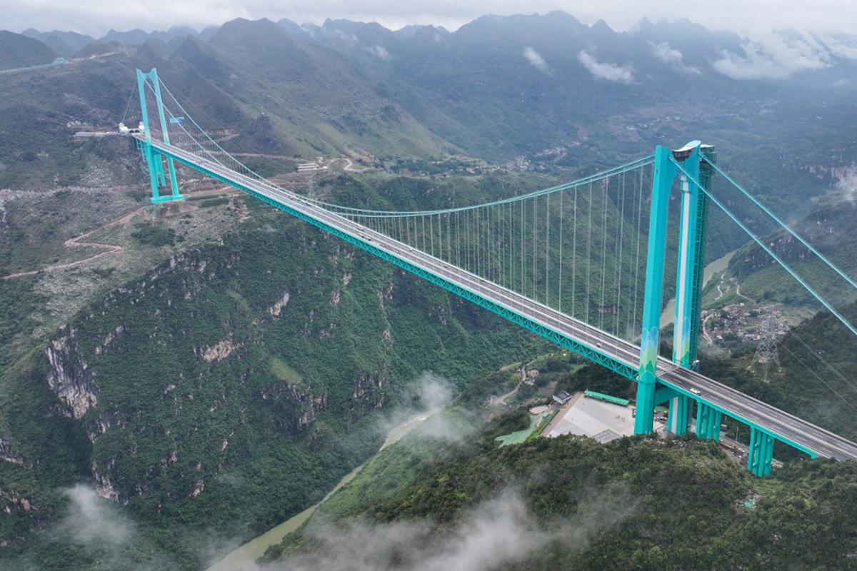 Photo en vue aérienne du pont suspendu bleu permettant de traverser un profond canyon dans un paysage montagneux.