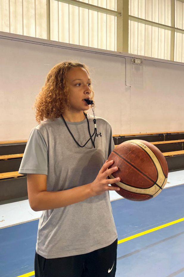 Nawres, sur un terrain de basket, un un ballon dans les mains et s'apprête à sifflet. 