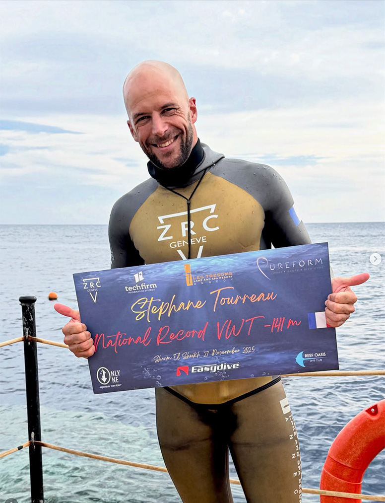 Photo de Stéphane Tourreau en combinaison de plongée et tenant entre ses mains une sorte de poster attestant qu'il a battu le record de France de plongée en apnée.