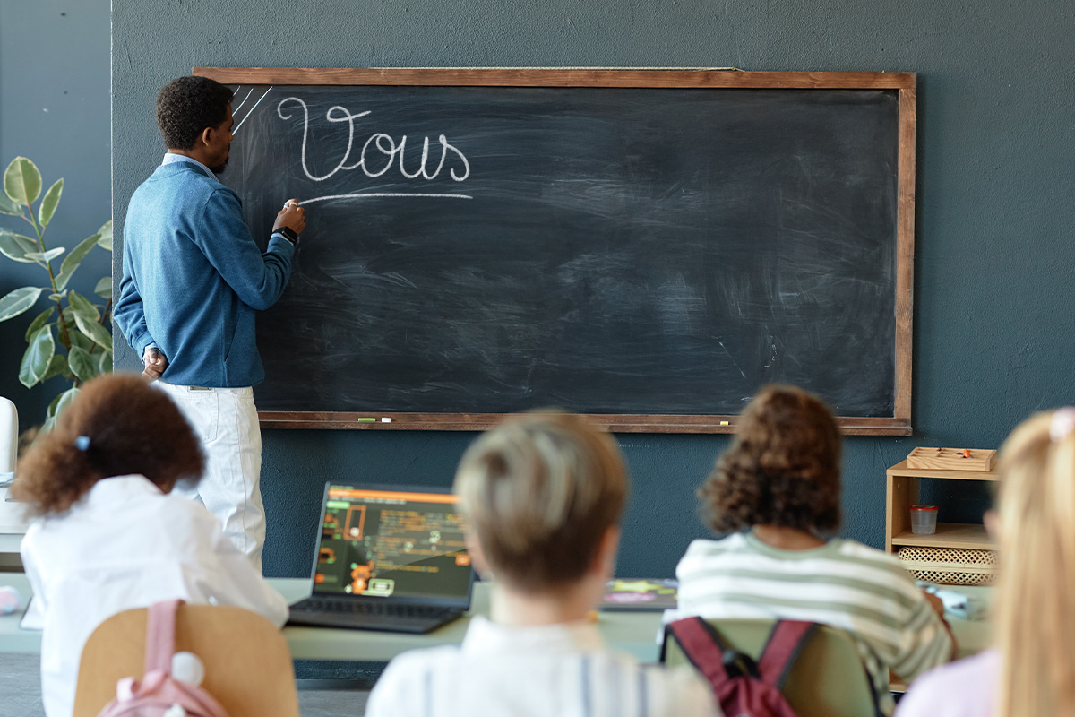 Un professeur écrit la mention "vous" sur le tableau face à ses élèves.