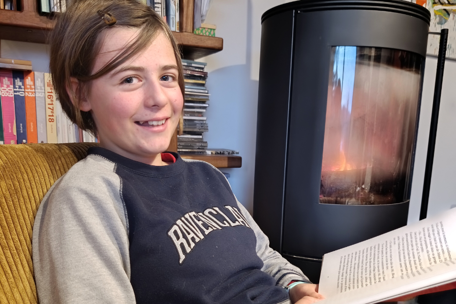 Mona, assise dans un canapé, devant un poêle, lis un livre.