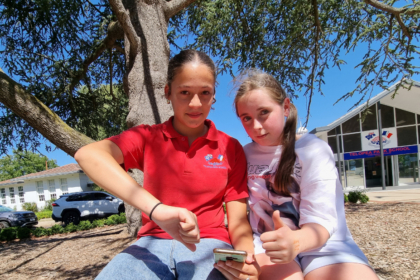 Omnia et Madeleine, assise sous un arbre. Omnia tient un portable, et fait un pouce en bas pour dire qu'elle n'approuve pas cette loi, et Madeleine fait un pouce en haut pour dire qu'elle, elle l'approuve.
